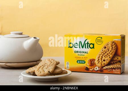 Tiraspol, Moldavia - 31 gennaio 2023: Belvita colazione scatola biscotti con miele smak e noci con choc chips, biscotti sul piatto e teiera su arancia ba Foto Stock