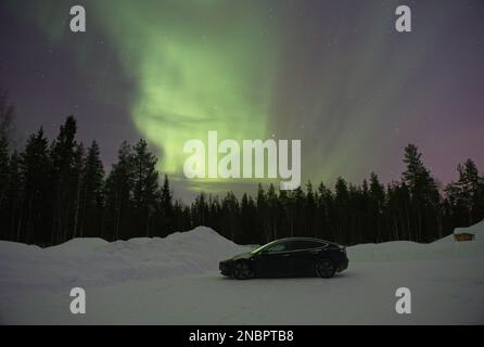 Kittila, Finlandia - 12 febbraio 2023: Paesaggi meravigliosi in Lapponia, Finlandia. Una Tesla modello 3 di colore nero pieno sotto la bella aurora boreale Foto Stock