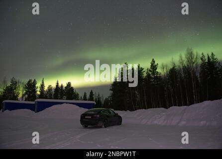 Kittila, Finlandia - 12 febbraio 2023: Paesaggi meravigliosi in Lapponia, Finlandia. Una Tesla modello 3 di colore nero pieno sotto la bella aurora boreale Foto Stock