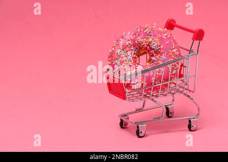 Ciambella con glassa rosa e zucchero multicolore spruzzate nel carrello della spesa su sfondo rosa Foto Stock