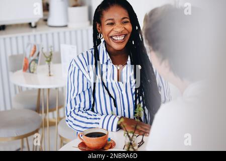 Allegra giovane donna d'affari sorridente felice durante una riunione di caffè con un collega in un caffè. Due donne d'affari che hanno una conversazione amichevole dentro Foto Stock