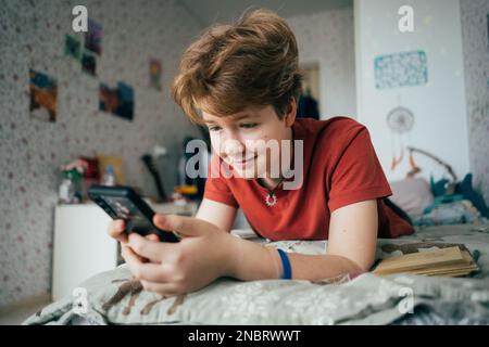 Ragazza adolescente sdraiata sul letto scrive messaggi sul telefono. Foto Stock