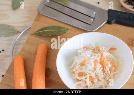 Home crauti con carote e spezie su un piatto, crauti. Insalata mista di verdure fresche in un piatto con forchetta su fondo di legno. Foto Stock