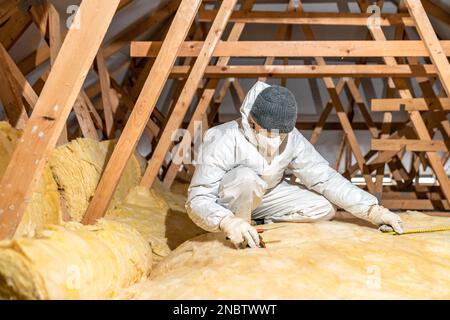 l'uomo isola il tetto e il soffitto della casa con lana di vetro Foto Stock