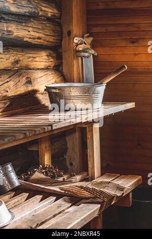 Interno di una tradizionale sauna in legno con secchio e mestolo in metallo posti su una panca in legno. Atmosfera accogliente e rustica tipica della Scandinavia, del Baltico Foto Stock