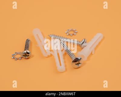 Viti e tasselli in plastica su sfondo arancione. Bulloni e perni di riferimento. Foto Stock