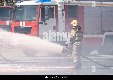 I vigili del fuoco spengono un incendio provocato da un camion antincendio. forte flusso di acqua e schiuma dalla manichetta antincendio in mano al pompiere. estinguere il fuoco con Foto Stock