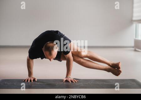 Un uomo di costruzione atletica fa yoga in palestra su un tappetino. Foto Stock