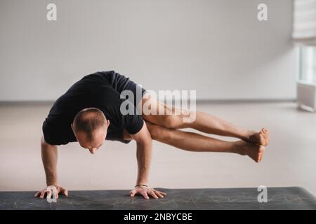 Un uomo di costruzione atletica fa yoga in palestra su un tappetino. Foto Stock