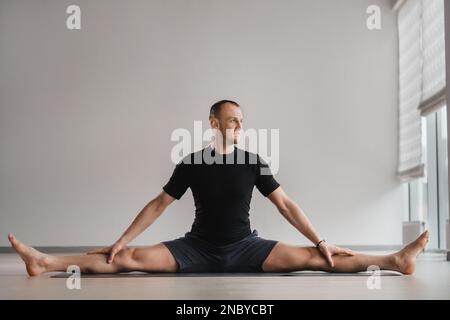 Un uomo di costruzione atletica fa yoga in palestra su un tappetino. Foto Stock