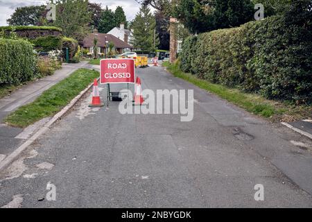 Un cartello stradale chiuso su una strada extraurbana britannica. Le barriere gialle circondano un buco scavato nello sfondo. Il cartello è accanto a tre coni stradali. Foto Stock