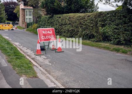 Un cartello stradale chiuso su una strada extraurbana britannica. Le barriere gialle circondano un buco scavato nello sfondo. Il cartello è accanto a tre coni stradali. Foto Stock