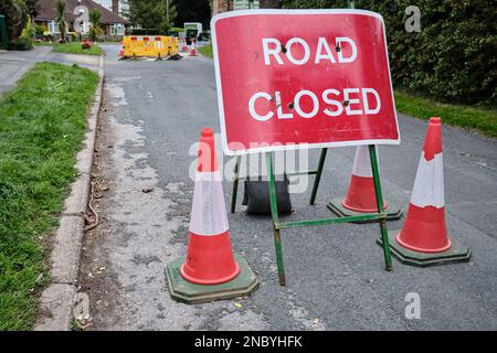 Un cartello stradale chiuso su una strada extraurbana britannica. Le barriere gialle circondano un buco scavato nello sfondo. Il cartello è accanto a tre coni stradali. Foto Stock