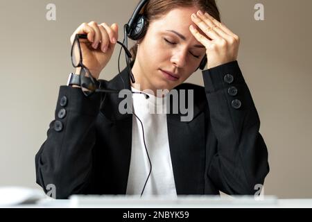 Esausta giovane donna consulente del call center che ha dura giornata sul lavoro, malattia mentale, mal di testa, affaticamento. Foto Stock