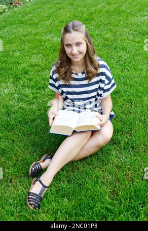 Bella giovane donna che legge un libro seduto sul prato verde Foto Stock