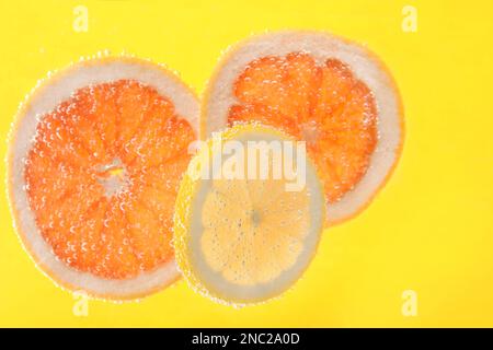 Fette di agrumi diversi in acqua frizzante su fondo giallo Foto Stock