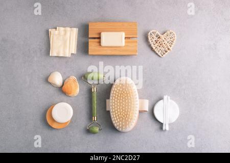 Composizione Knolling con prodotti per la cura del sé su sfondo grigio. Sapone per il corpo, spazzola per massaggio a secco, batuffoli di cotone, rullo di giada su sfondo grigio. Foto Stock