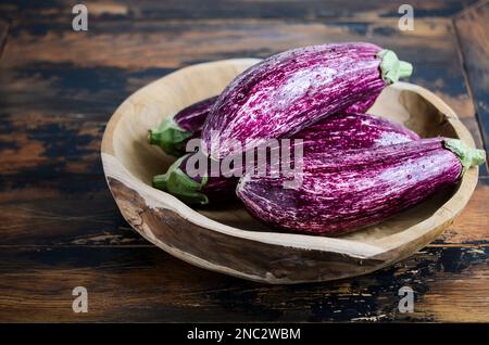 Melanzane di Graffiti biologiche fresche in una ciotola di legno su fondo di cemento. Foto Stock