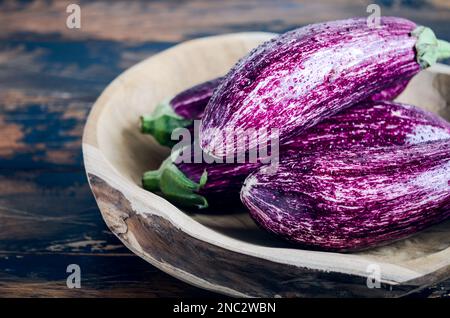 Melanzane di Graffiti biologiche fresche in una ciotola di legno su fondo di cemento. Foto Stock