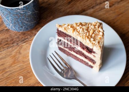 Una fetta di burro di arachidi appena sfornato e torta al cioccolato. La torta ha un denso ripieno di crema di burro e viene servita su un piatto laterale con una tazza di tè Foto Stock