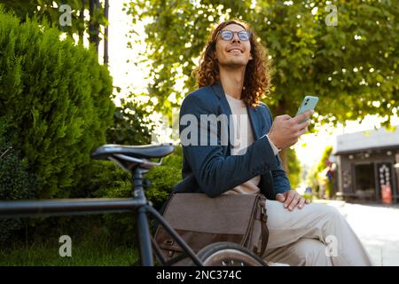 Zenzero uomo europeo utilizzando il telefono cellulare mentre si siede in bicicletta nel parco cittadino Foto Stock