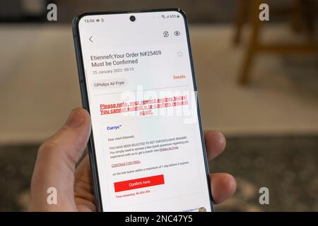 Una mano che tiene in mano uno smartphone con un falso messaggio di phishing Currys da parte di truffatori, Inghilterra. Concetto: E-mail fraudolente, e-mail fraudolente, e-mail truffa, frodi nel Regno Unito Foto Stock