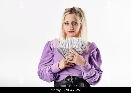 Giovane bella donna che indossa la blusa a coste lilla isolato su sfondo bianco tenendo le banconote vicino al petto, ride e guarda la fotocamera. Ama m. Foto Stock