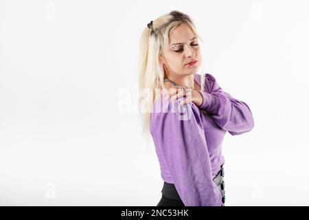 Giovane bella donna che indossa la blusa a coste lilla isolato su sfondo bianco facendo auto massaggio al collo e alle spalle. Grave dolore alla spalla e ve Foto Stock