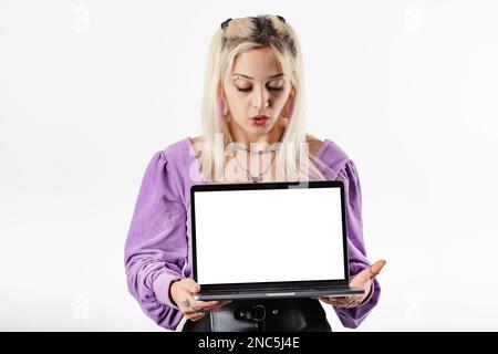 Bella donna bionda che indossa una blusa a coste isolata su sfondo bianco tenendo un notebook con uno schermo bianco fissa lo schermo o Foto Stock