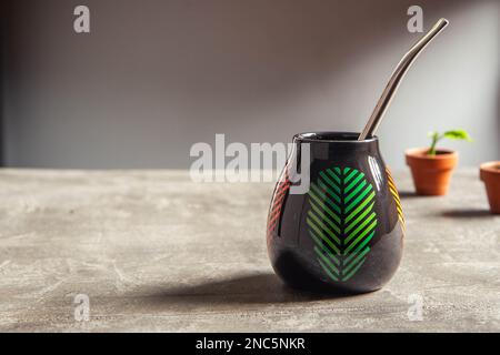 tazza di yerba mate in ceramica piuttosto lucida, con design a foglia verde e paglia di metallo bombarbilla su un tavolo da banco in cemento Foto Stock