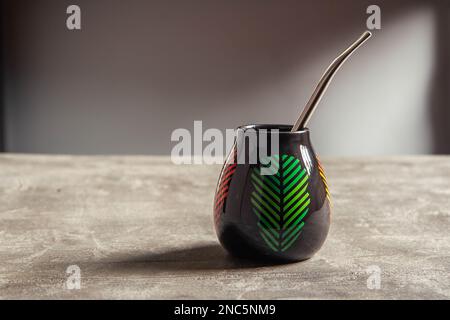 tazza di yerba mate in ceramica piuttosto lucida, con design a foglia verde e paglia di metallo bombarbilla su un tavolo da banco in cemento Foto Stock