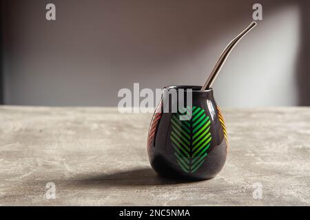 tazza di yerba mate in ceramica piuttosto lucida, con design a foglia verde e paglia di metallo bombarbilla su un tavolo da banco in cemento Foto Stock