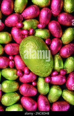 Mucchio di diversi colori e diverse misure di foglio colorato avvolto cioccolato uova di pasqua in rosa, e verde, con un grande uovo verde lime. Foto Stock