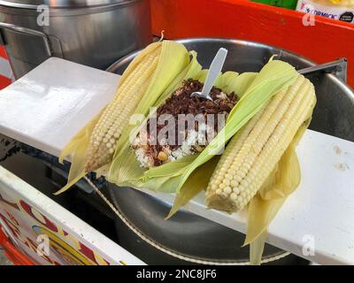 Esquites, un cibo di strada tradizionale messicano, un carrello di strada a Oaxaca, Messico, guarnito con cappuline o cavallette arrostite. Foto Stock