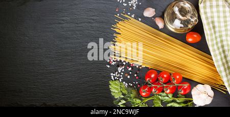 Pasta, spaghetti e ingridienti da cucina su superficie nera in ardesia. Concetto di cucina italiana, menu del ristorante, modello di ricetta. Vista dall'alto, piatto, mockup Foto Stock