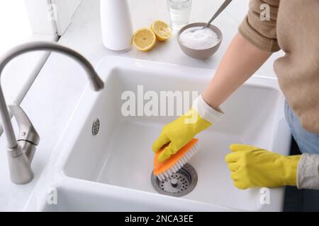 Donna che usa bicarbonato di sodio e spazzola per pulire lavello, primo piano Foto Stock