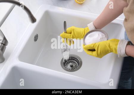 Donna che usa bicarbonato di sodio per disintasare lo scarico del lavandino, primo piano Foto Stock