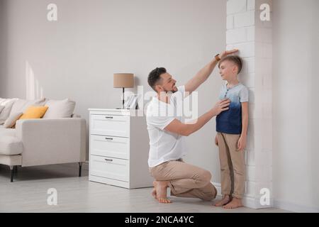 Padre che misura l'altezza del figlio vicino al muro di casa Foto Stock