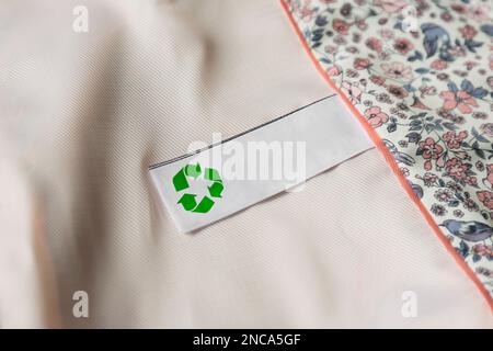 Etichetta di abbigliamento con il simbolo di riciclaggio su un indumento leggero, primo piano Foto Stock