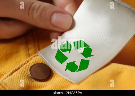 Donna che mostra l'etichetta di abbigliamento con il simbolo di riciclaggio su jeans gialli, primo piano Foto Stock