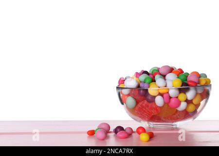 Molte caramelle diverse in ciotola di vetro su tavolo di legno rosa su sfondo bianco Foto Stock