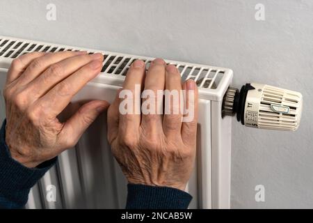 Le mani dell'uomo anziano che cerca di mantenere caldo sul radiatore di riscaldamento. Primo piano. Foto Stock