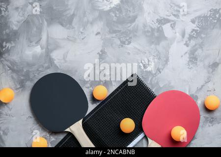 Racchette da ping pong, rete e palle su tavolo grigio, piatto. spazio per il testo Foto Stock