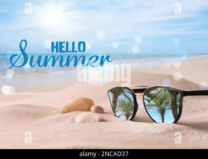 Ciao estate. Occhiali da sole sulla spiaggia di sabbia con conchiglie vicino al mare Foto Stock