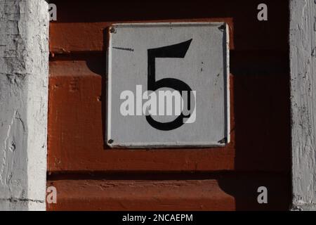 Casa numero cinque. scritta nera in metallo su sfondo bianco su una parete di legno rosso Foto Stock