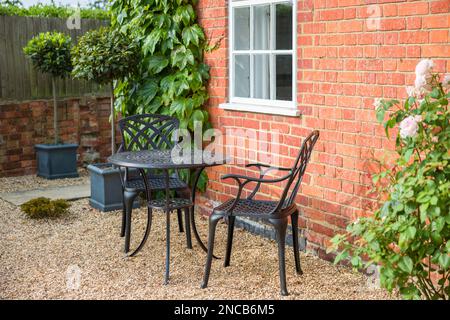 Giardino paesaggistico con tavolo da bistro e sedie su ghiaia nel tradizionale giardino britannico Foto Stock