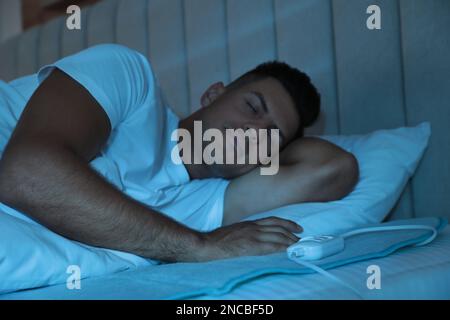 Uomo che dorme sul cuscino riscaldante elettrico a letto di notte Foto Stock