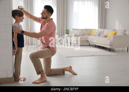 Padre che misura l'altezza del figlio vicino al muro di casa Foto Stock