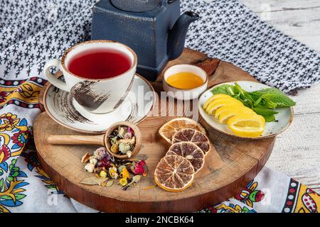 Teiera blu in ghisa. Bastoncini di cannella, nome, fettine di limone e zenzero essiccato su un tagliere. Ancora vita. Set di tè in ghisa con diverse erbe f Foto Stock