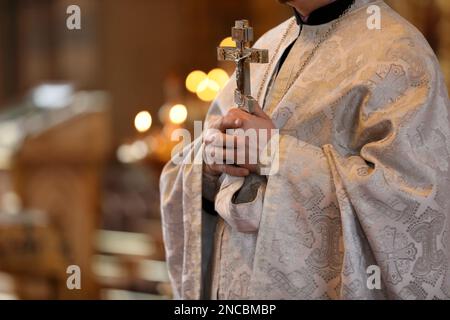 Sacerdote che tiene la croce in chiesa durante la cerimonia del battesimo, primo piano Foto Stock